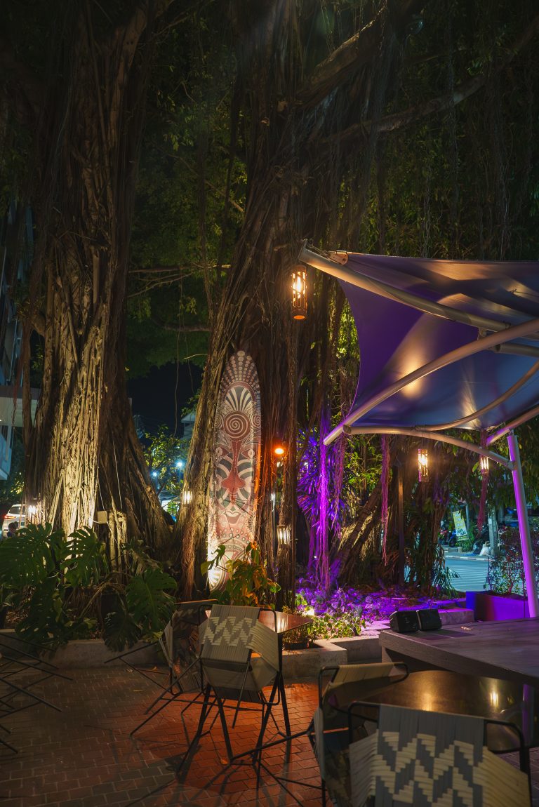 Espace de sièges extérieur illuminé la nuit avec des arbres Banyan, parfait pour un bar extérieur.
