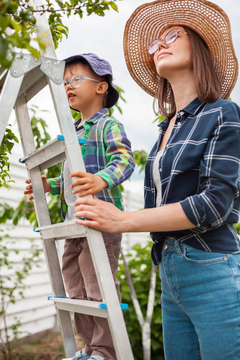 Mère et enfant sur une échelle près d'un arbre, jardinant dans le jardin arrière