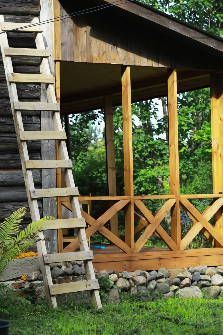 Échelle en bois rustique appuyée contre un chalet à la campagne avec porche et fondation en pierre dans la nature