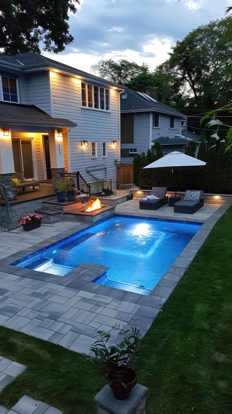 Une grande maison grise avec une piscine dans le jardin, entourée d'arbres et de buissons verdoyants.